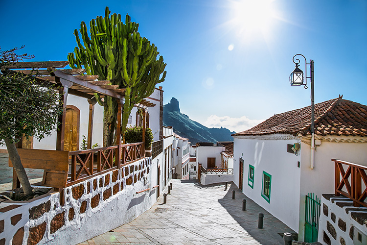 Imagen de una calle de Tejeda, uno de los pueblos más bonitos de España. Suelo empedrado, paredes blancas y barandas de madera.