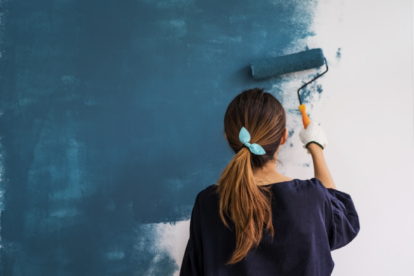 Mujer pintando la pared, cambiando el color de blanco a azul