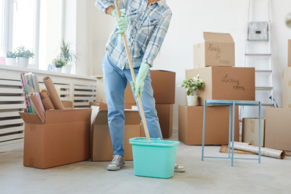 Imagen de una mujer con un cubo y una fregona, entre cajas, limpiando después de la mudanza