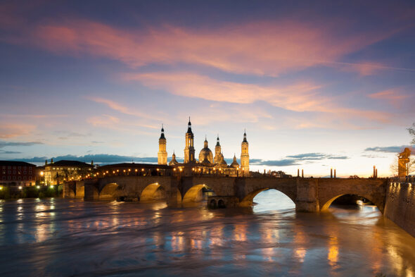 Zaragoza al atardecer, con su puente en primer plano sobre el río y la catedral al fondo