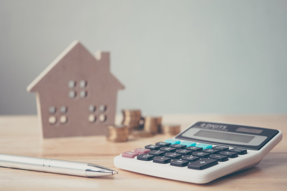 Calculadora y casa de madera en miniatura, representando la compraventa de viviendas