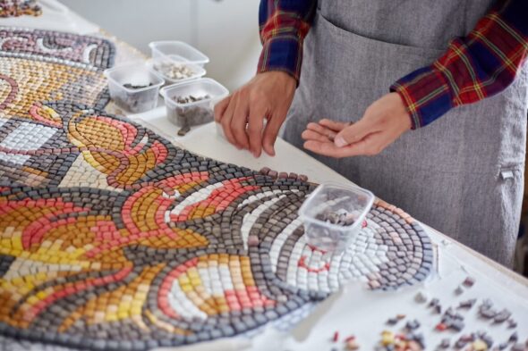 Manos preparando piezas para rellenar una mesa de mosaico en colores rojo, amarillo y gris