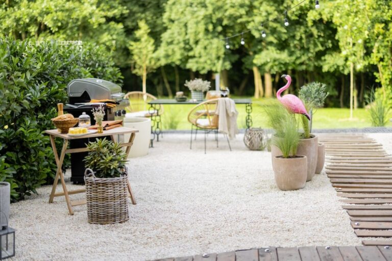 Zona de barbacoa con suelo de piedras y fondo verde con árboles