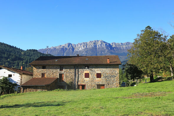 Casa rural de piedra con montañas de fondo y campo verde