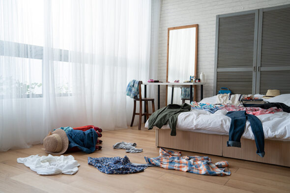 Habitación con la cama llena de ropa y mucho desorden